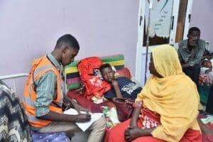 Healthcare worker noting patient details with woman and child during medical aid efforts, supported by ETH donations for general healthcare.