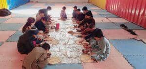 Children eating a meal on the floor, showing communal dining and food aid in crisis zones, supported by crypto donations via USDT.