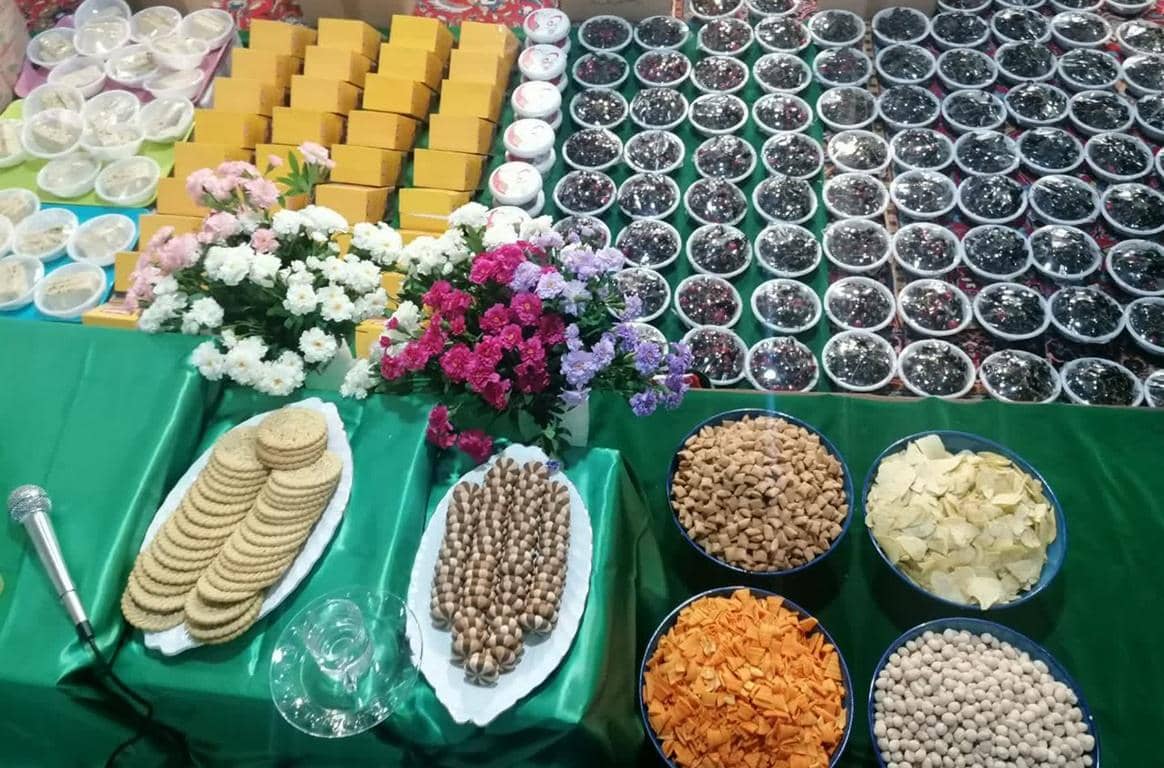 Zakat al-Fitr 2026 preparations featuring rows of food items for charity, including cookies, nuts, and sweets, with floral decorations and a microphone, symbolizing the distribution of essential items through crypto donations like USDT.