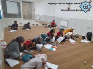 Children sitting on the floor engaging in educational activities, supported by crypto donations, including an illustration of a child learning with BTC.