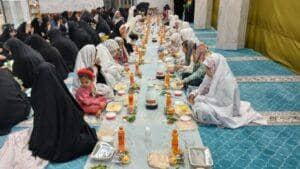 Group of Muslim women and children gathered for Iftar, sharing a communal meal with food laid out on mats. This scene represents the spirit of Zakat al-Fitr and community bonding, with donations facilitated by cryptocurrency like Bitcoin.