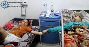 Two children lie in hospital beds, one smiling and holding the other's hand, symbolizing hope and resilience in care supported by BTC donations.