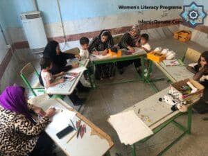 Women's Literacy Programs class in session, possibly funded by BTC donations, showing children and adults learning and creating art. IslamicDonate.Com logo visible.
