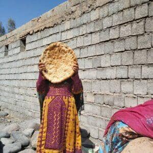 A woman in traditional clothing holds flatbread in front of her face. This symbolizes the need for basic supplies and aid for women in crisis, supported by crypto donations like SOL.