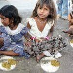 Three young children sitting on the ground with bowls of food, one girl in a blue dress, the other in a white top. Crypto donations via USDT support this relief.
