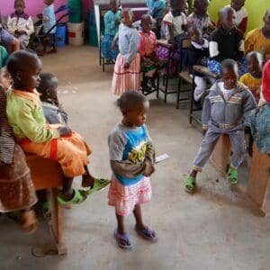 A group of orphaned children sit and stand, receiving educational support through crypto donations, including 49 children sponsored in the 2023-2024 academic year, with an emphasis on ETH-supported aid.