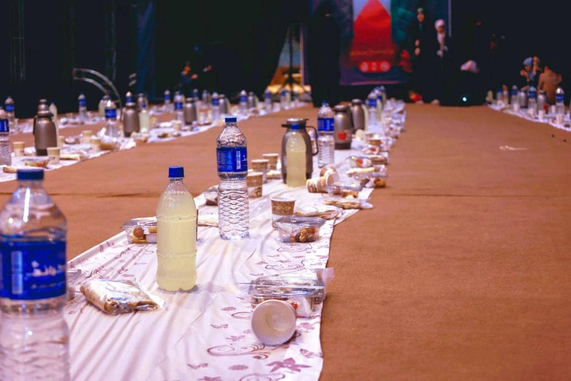 Ramadan iftar meals set up on a long table with bottles of water and drinks, implying crypto donations enable this feast for the needy, possibly using ETH to facilitate aid.
