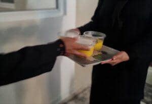 Person receiving tray with three cups of yellow liquid, celebrating Prophet's birthday with crypto donations, possibly via RLUSD, embodying generosity and community spirit.