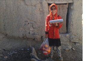 Smiling girl in headscarf holding books and a bag of fruit, supported by BTC crypto donations for a stronger Muslim community. Celebrating Prophet's birthday with generosity.