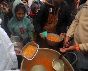 Children and adults receiving portions of food from a large communal pot, highlighting humanitarian aid efforts in Gaza, supported by crypto donations via AED.