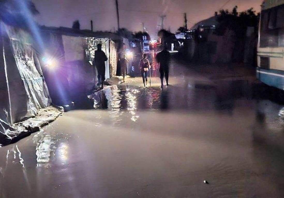 People walk through flooded streets near makeshift shelters at night, aided by crypto donations via USDT for winter relief.