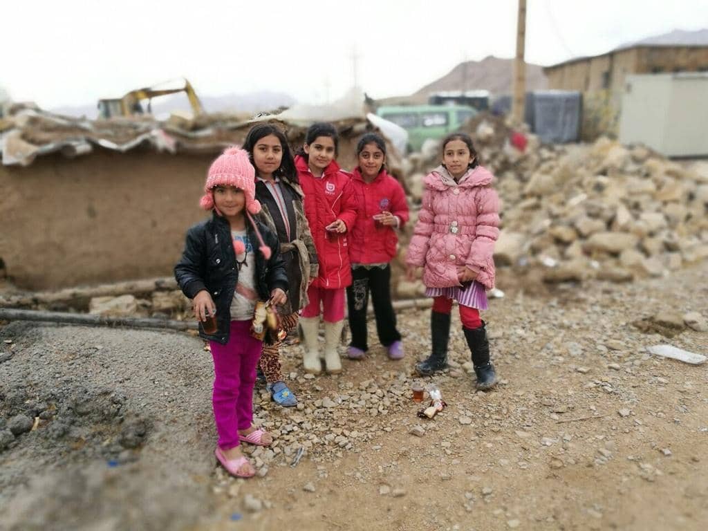 Children in winter coats stand near damaged shelters, receiving aid through crypto donations like BTC, providing warmth and hope.