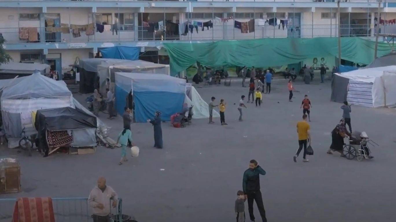 Camp residents in makeshift shelters receive aid, with a person in a wheelchair being pushed, symbolizing the urgent need for crypto Zakat donations in Palestine.