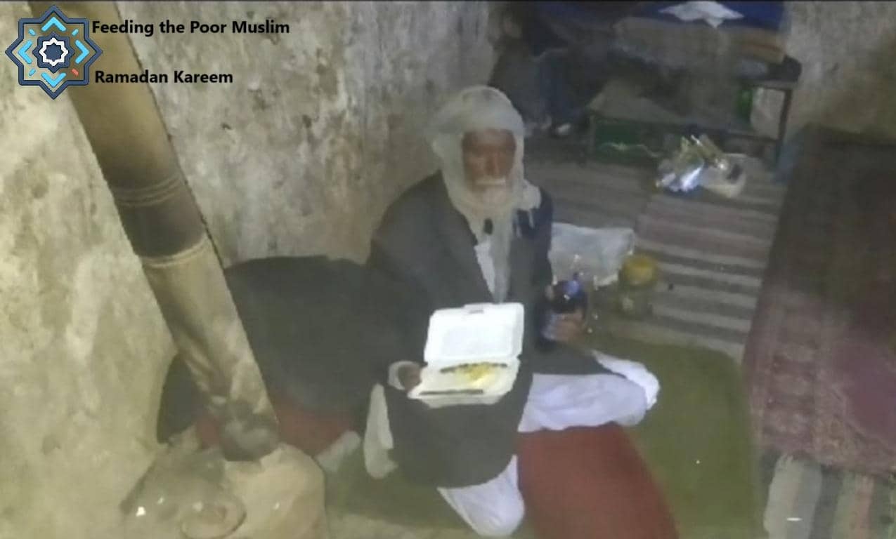 An elderly Muslim man sits on the floor in a humble dwelling, holding a food container. He receives aid through crypto zakat donations, exemplified by BTC.
