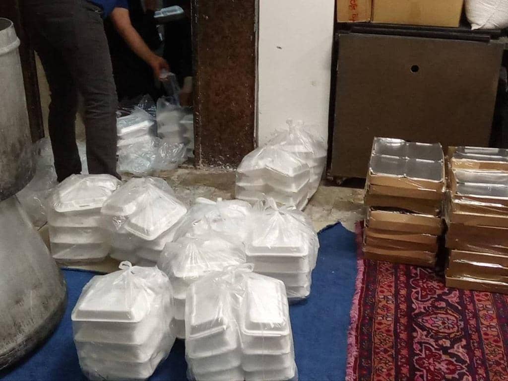 Stacks of white food containers prepared for distribution, implying crypto-supported aid. Bags of containers shown with one being handled by a person. Crypto zakat donation for needy families.