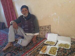 Elderly man sitting on a carpet with three containers of food and bread. Humanitarian aid is provided via crypto donations, such as BTC.