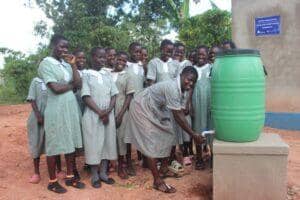 Ugandan schoolchildren gather around a green water barrel as one student dispenses clean water, symbolizing hope and relief aided by Solana donations.
