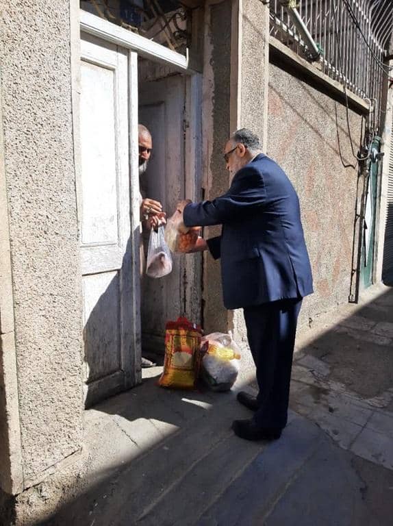 Elderly man in a suit hands groceries through a doorway to another man. Donation made via ETH.