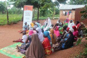 Islamic Donate banner behind a group of people, mostly women and children, gathered outdoors in a village setting. This scene depicts community aid and support, with donations potentially facilitated by crypto, such as BNB.
