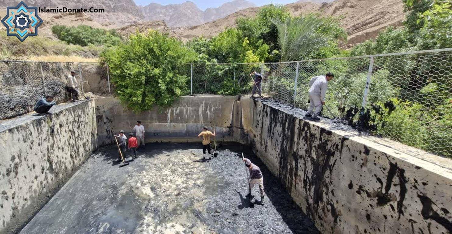 Men working to clean a concrete water reservoir, a construction of Sadaqah Jariyah for clean water access and agriculture, supported by crypto donations like Bitcoin.