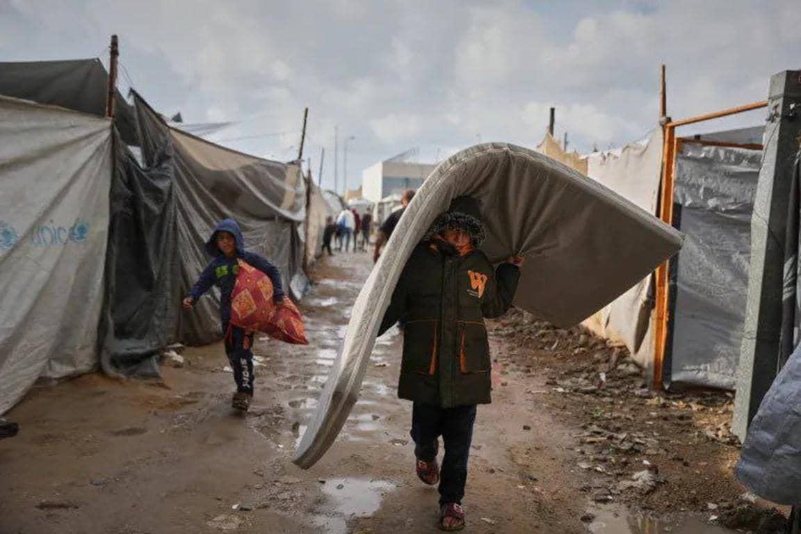 Children carrying a mattress and supplies through a muddy camp in Gaza during the urgent battle against winter crisis, aided by cryptocurrency donations like ETH.