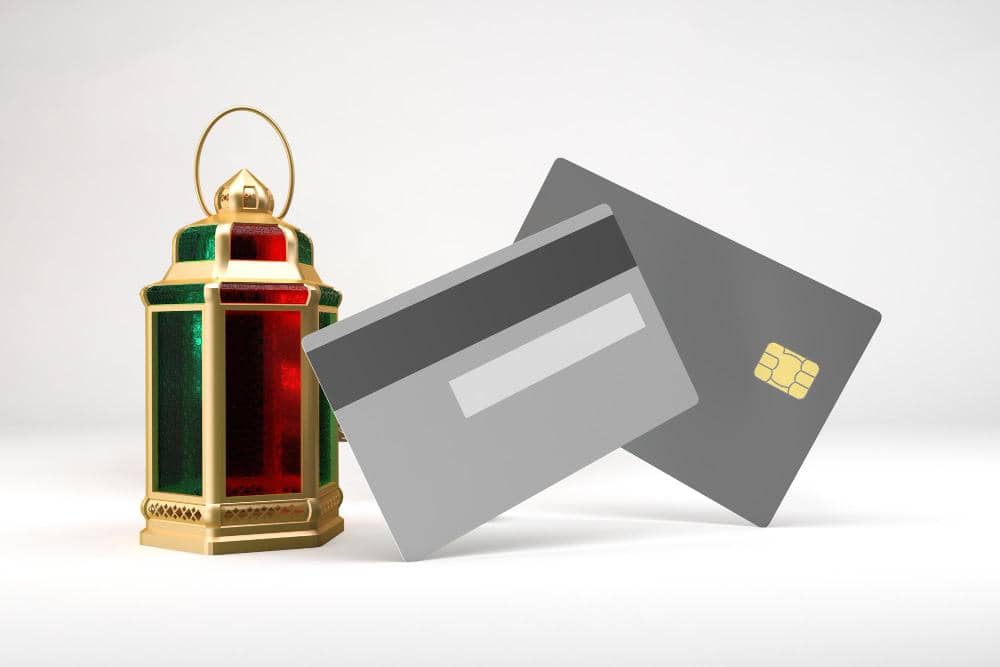A festive Ramadan lantern sits next to two credit cards, symbolizing modern ways to pay Sadaqa, with donations processed via Solana.
