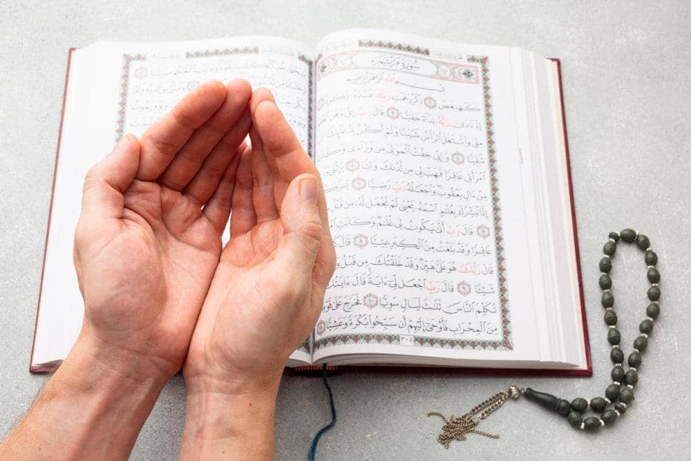 Open Quran with hands in prayer and prayer beads. Ramadan daily supplications, wisdom, forgiveness, mercy, guidance. ETH