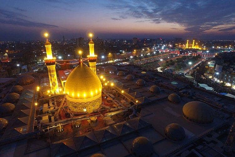 Imam Hussain Holy Shrine at dusk lit up with a golden dome and minarets. Pilgrims gathered outside. Donate with Bitcoin for secure, transparent giving.