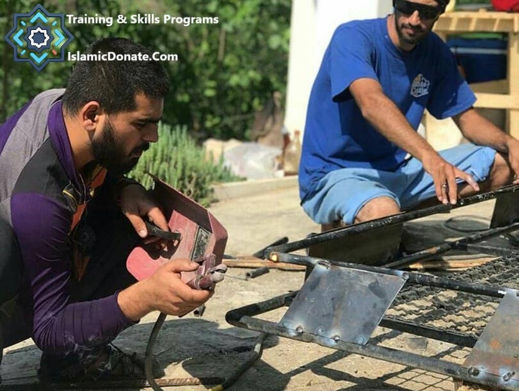 Two men engage in vocational training, with one welding metal. The image illustrates training and skills programs funded by cryptocurrency donations, supporting livelihoods.