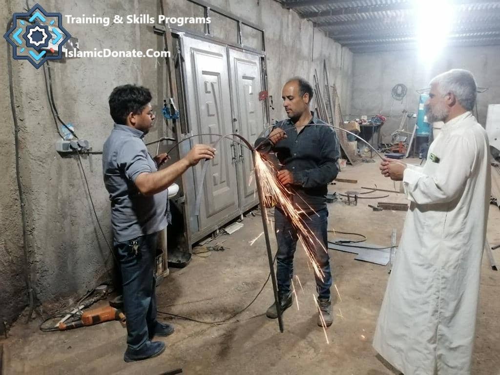 Three men in a workshop, two working on metal with sparks flying, illustrating training and skills programs funded by Sadaqah via cryptocurrency donations like RLUSD or PYUSD .