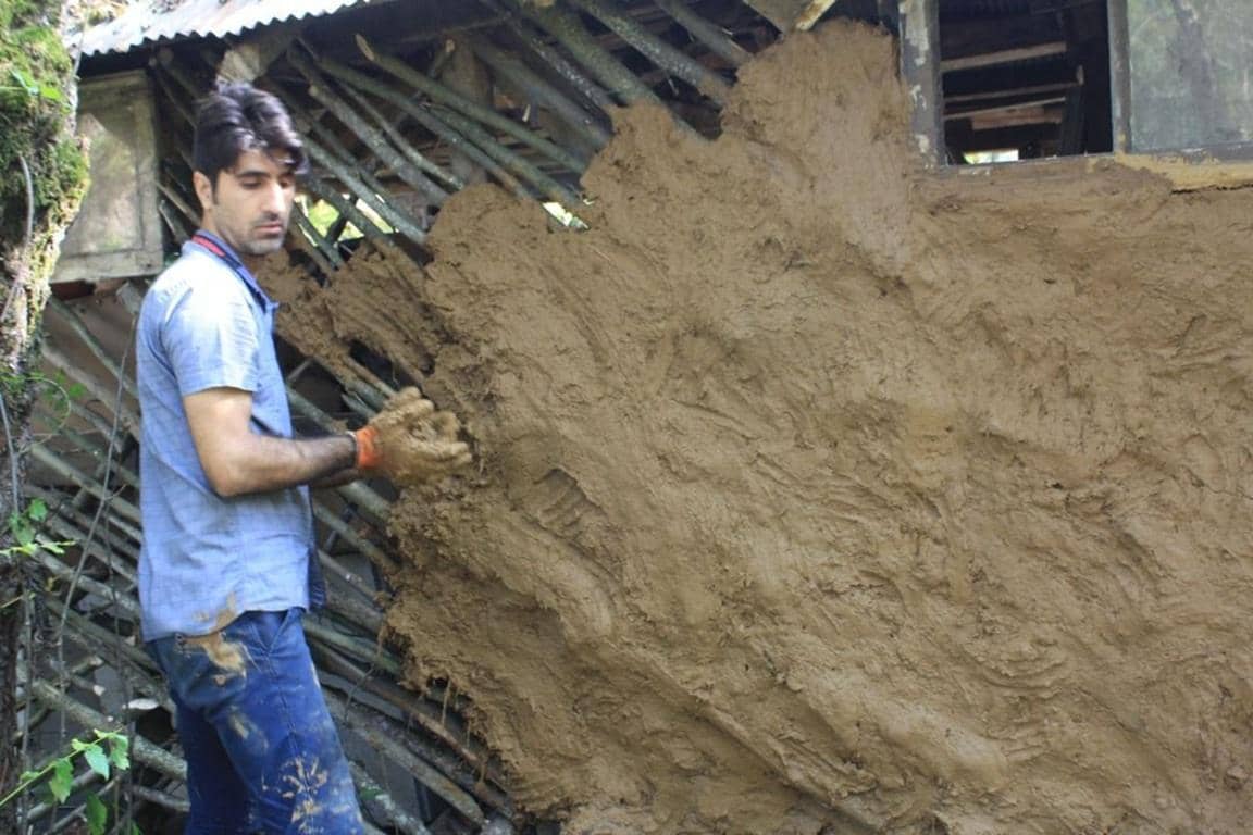A man applies mud to a structure as part of a skills workshop on construction and masonry, facilitated by crypto donations via BTC.