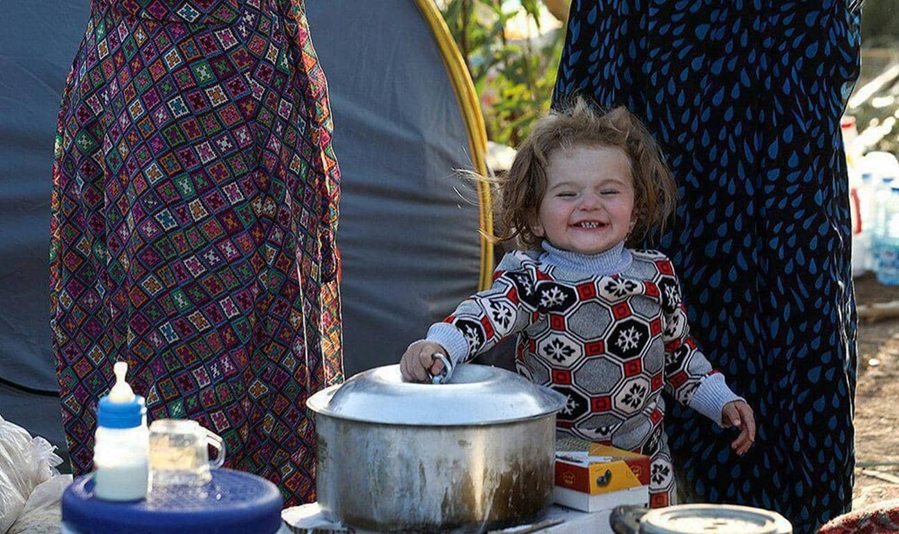 A joyful child smiles while helping lift the lid off a pot, possibly symbolizing food distribution aided by crypto donations like LTC, supporting impoverished families.