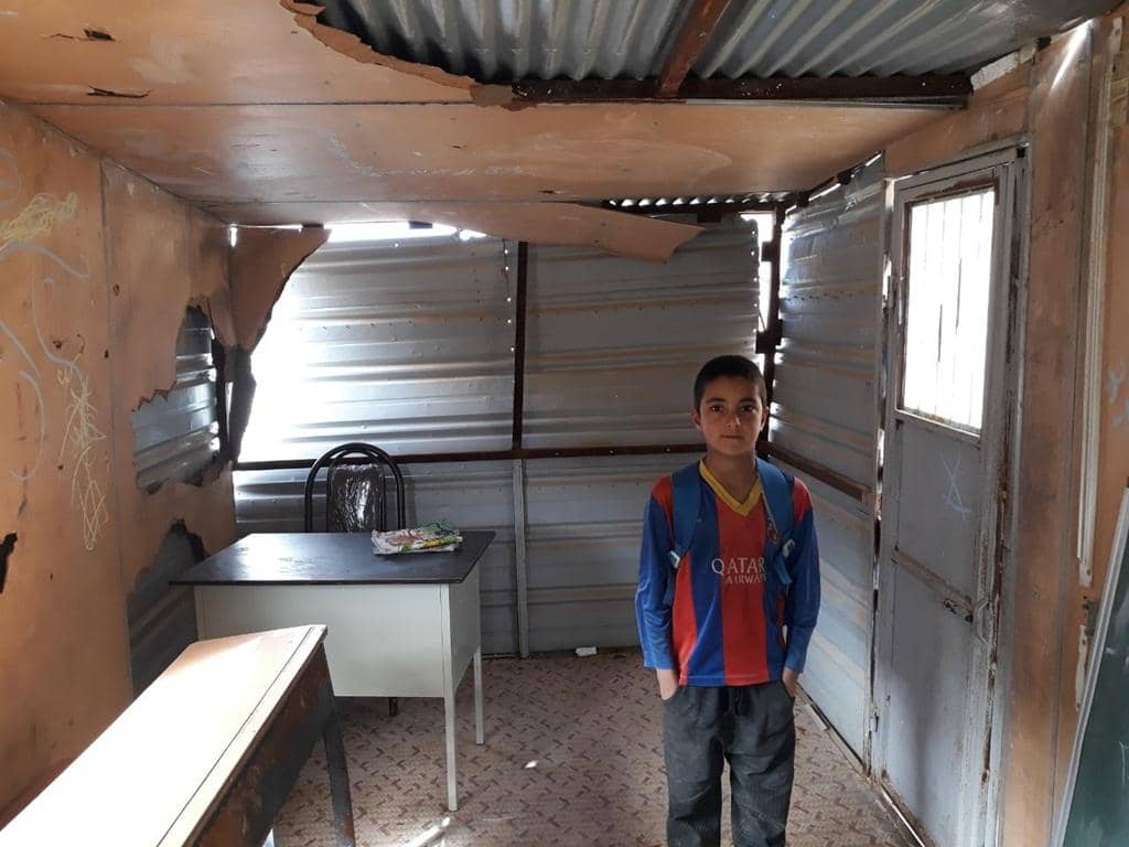 A young boy stands in a damaged classroom, a symbol of need. Your crypto donation, like Ethereum, supports education for orphans.