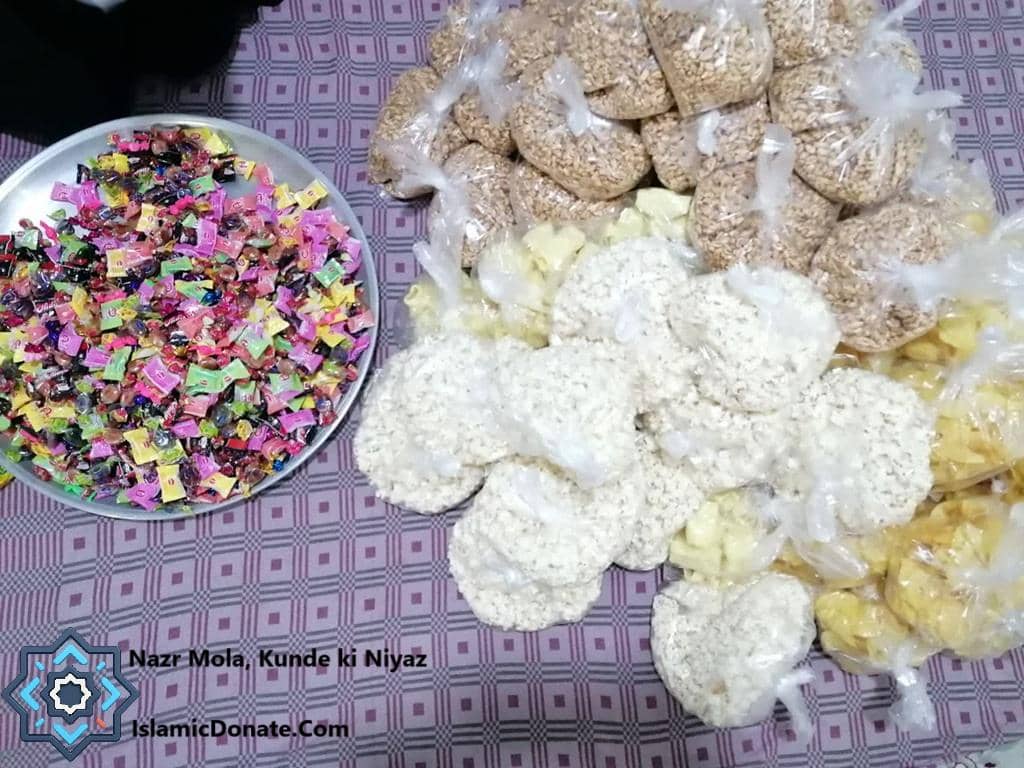 A platter of individually wrapped colorful candies sits next to large bags of dry goods, distribution during the Nazr Mola, Kunde ki Niyaz observance. Donate crypto for charitable offerings.