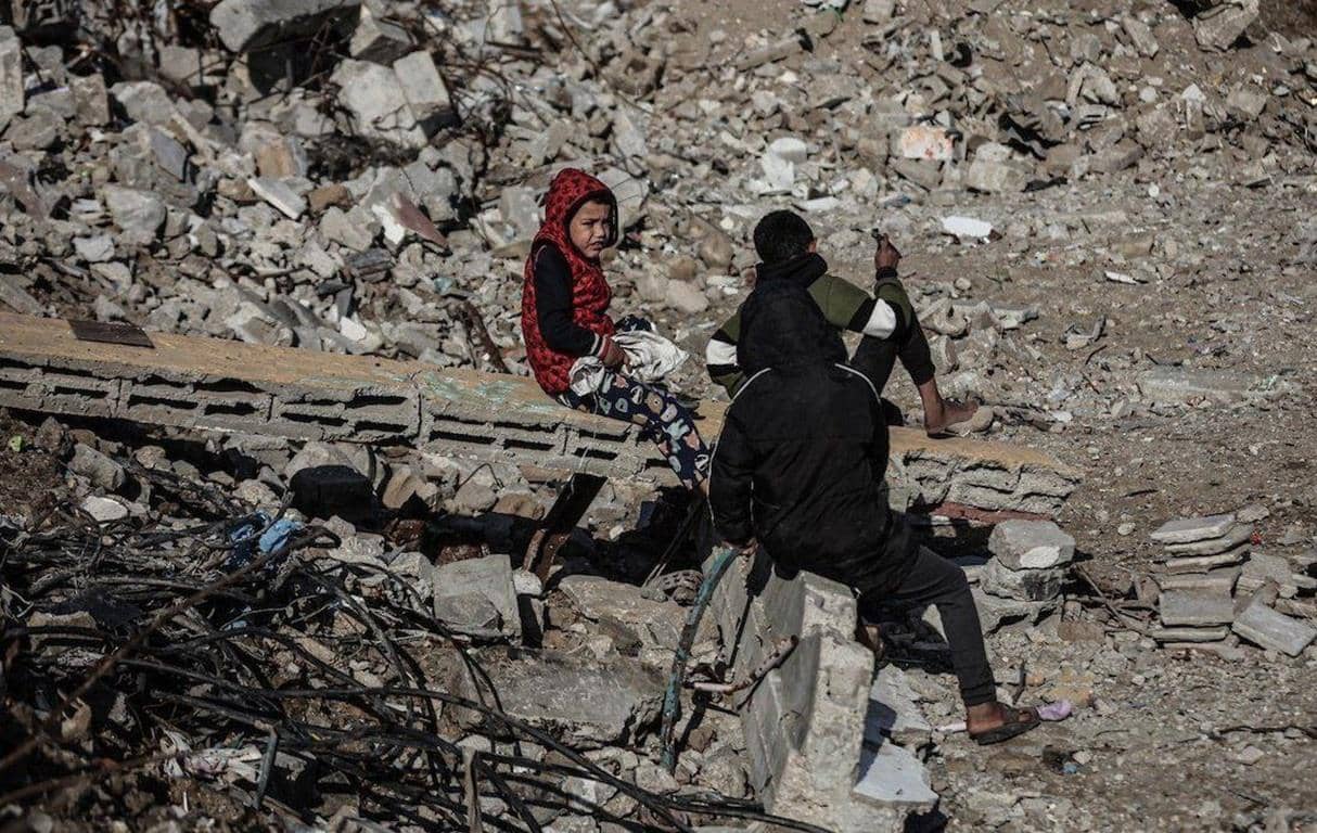 Children sit amidst rubble, highlighting the impact of conflict on the vulnerable. This image underscores the urgent need for humanitarian aid and symbolizes how crypto Khums donations, such as USDT, can provide essential support.