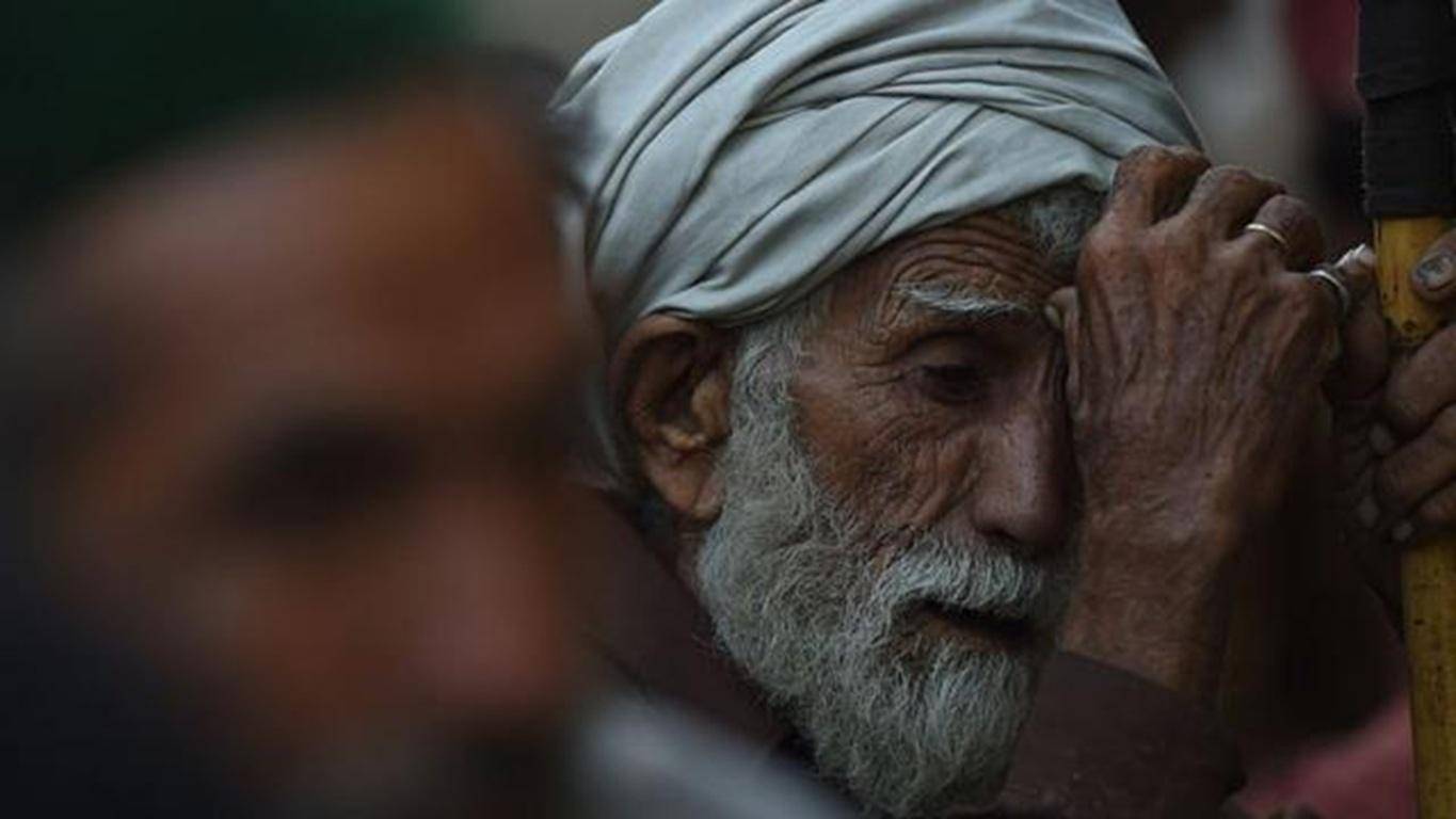 Elderly man in a turban with a gray beard, resting his head on his hands, conveying hardship, with the implication of aid via crypto donations like BTC.