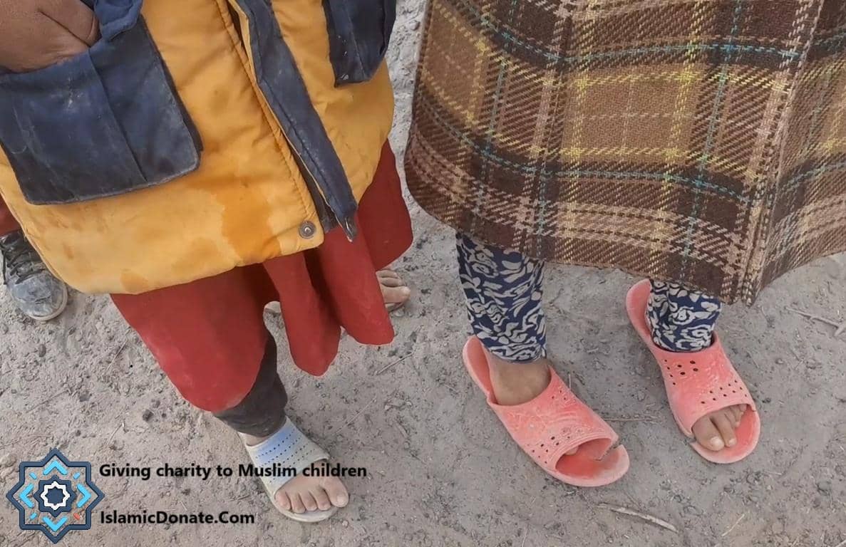 Childrens legs wearing worn clothing and sandals, representing recipients of Islamic charity donation via crypto. Supported by Ethereum.