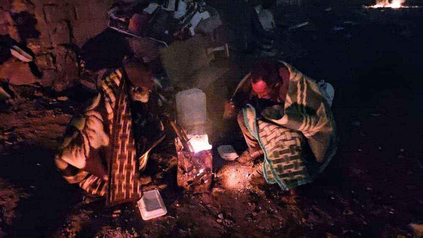 People huddled around a fire for warmth, receiving aid made possible by cryptocurrency donations like BTC, symbolizing how Zakat provides essential relief to the needy in impoverished regions.