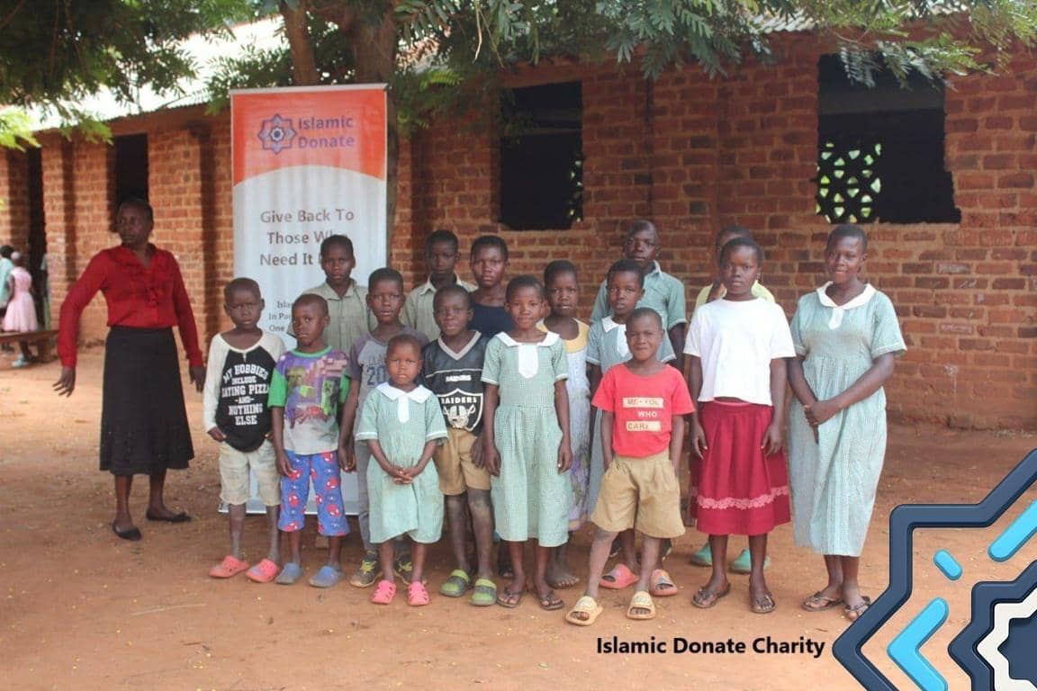 A diverse group of children and a woman stand in front of a brick building with an "Islamic Donate" banner. The children are smiling, and the woman appears to be a caregiver. Keywords: Zakat, Crypto, Donation, Charity, Children, Islamic Relief, Palestine, Yemen, Syria, Sudan, Gaza, Muslim Ummah, Humanitarian Aid. Ripple or Litecoin can be used for zakat.