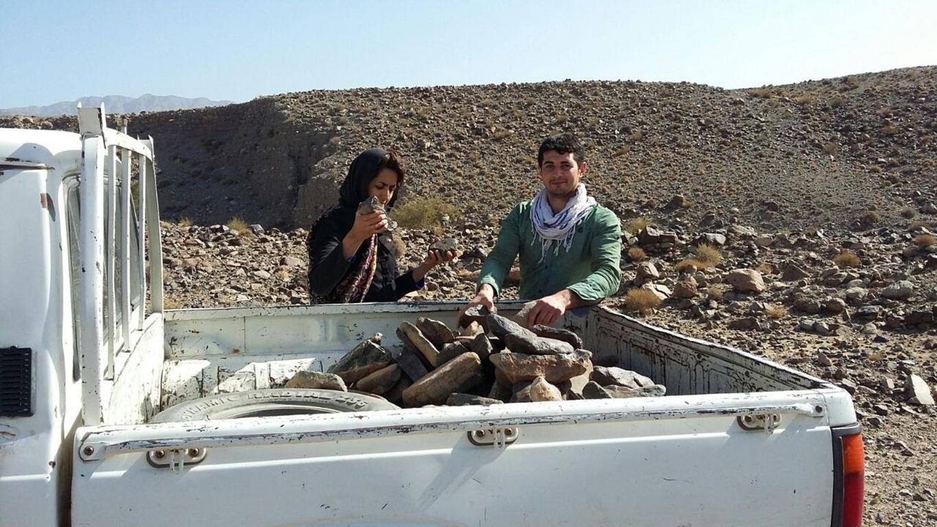 Two people loading stones into the back of a pickup truck in a rocky, arid landscape, hinting at manual labor for relief efforts supported by Dogecoin crypto donations.