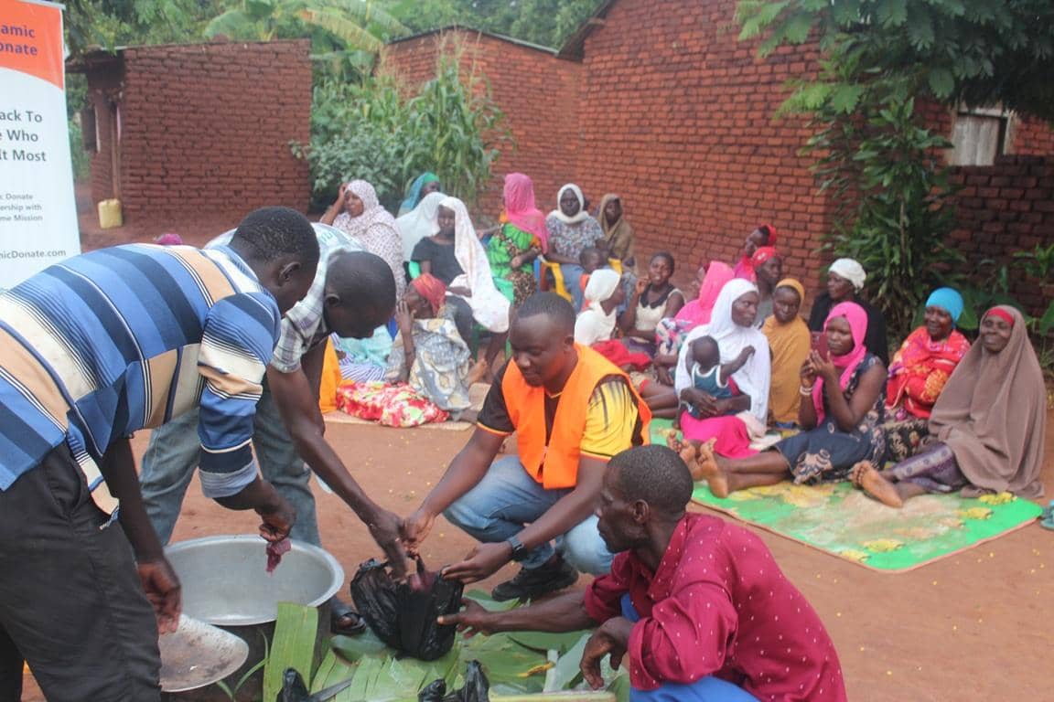 Men preparing meat for distribution to a seated group of women and children, representing community-based Islamic charity and Qurbani donations facilitated by cryptocurrency like Litecoin.