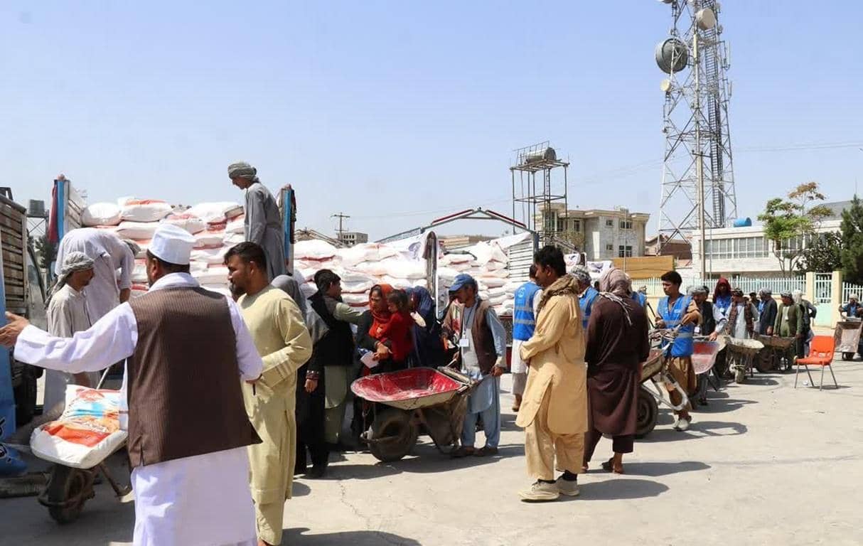Afghan people receiving aid, including food supplies and essential items, in a humanitarian effort supported by BTC donations. Relief efforts focus on earthquake victims, education, and protection needs.