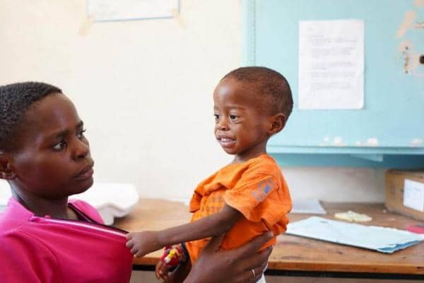 Child in an orange shirt held by an adult, receiving care. Support Ethiopian relief efforts with crypto donations like Bitcoin.
