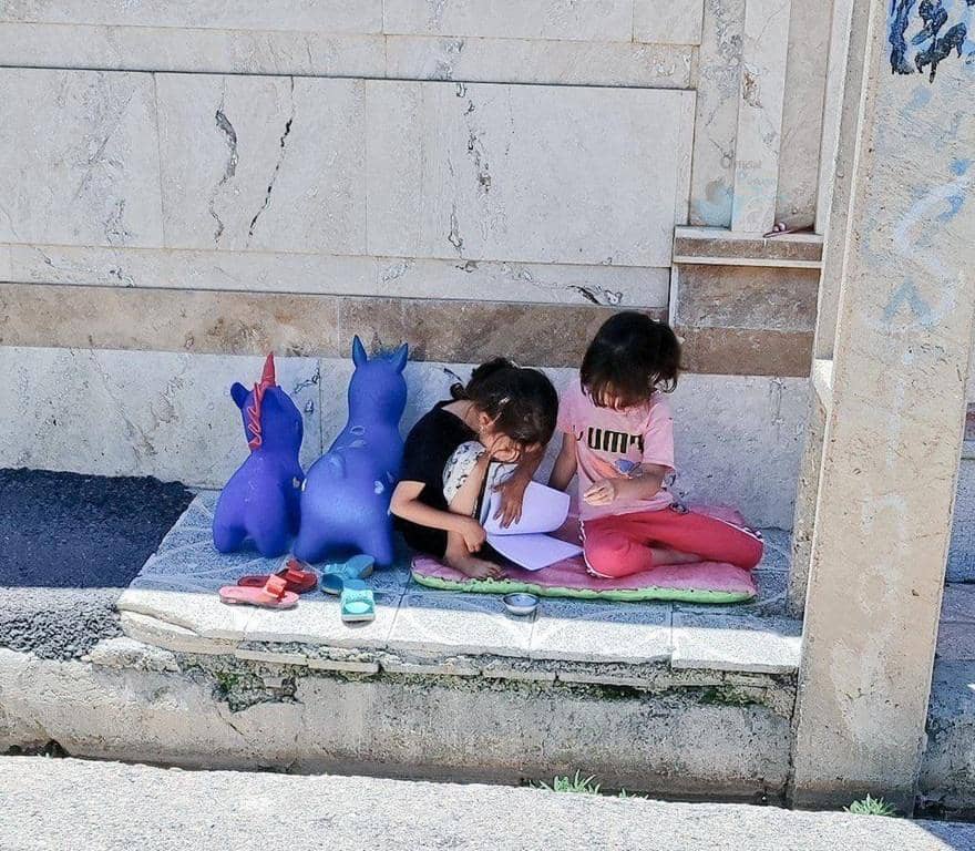 Two young girls study together outdoors, with two blue unicorn toys beside them, indicating potential for orphan sponsorship through crypto, supported by XRP.