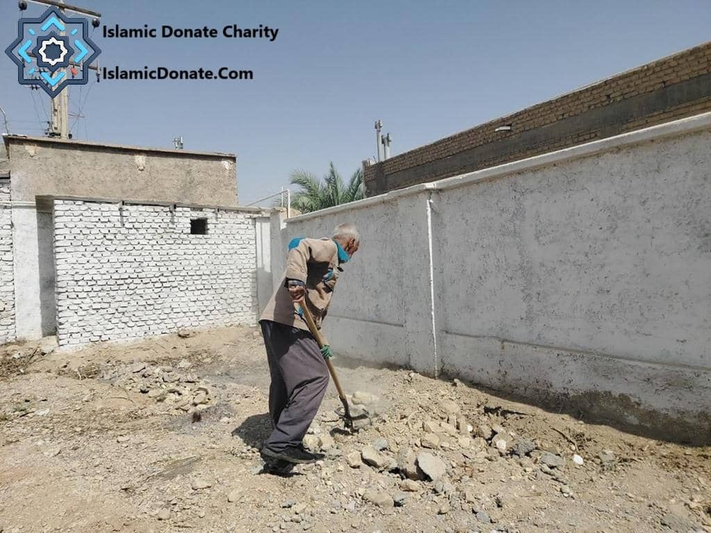 Elderly man digging with shovel, preparing soil for planting date trees in arid region, supported by crypto donations with ETH.