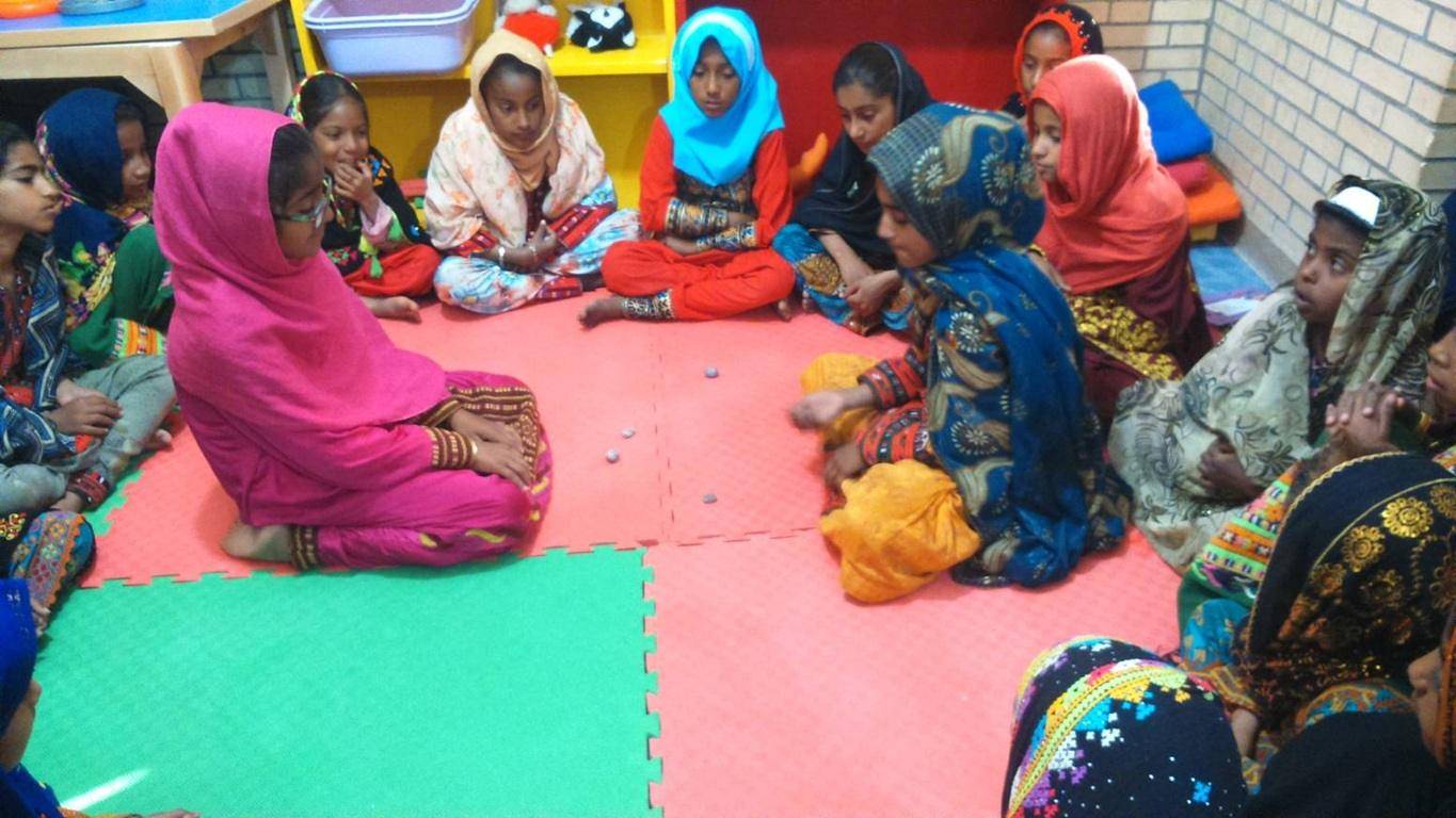 Group of young girls, some wearing hijabs, sitting in a circle on a padded floor, possibly in a classroom or community center, engaged in an activity. Their presence signifies hope and the positive impact of Islamic charity, potentially supported by crypto donations via USDT.