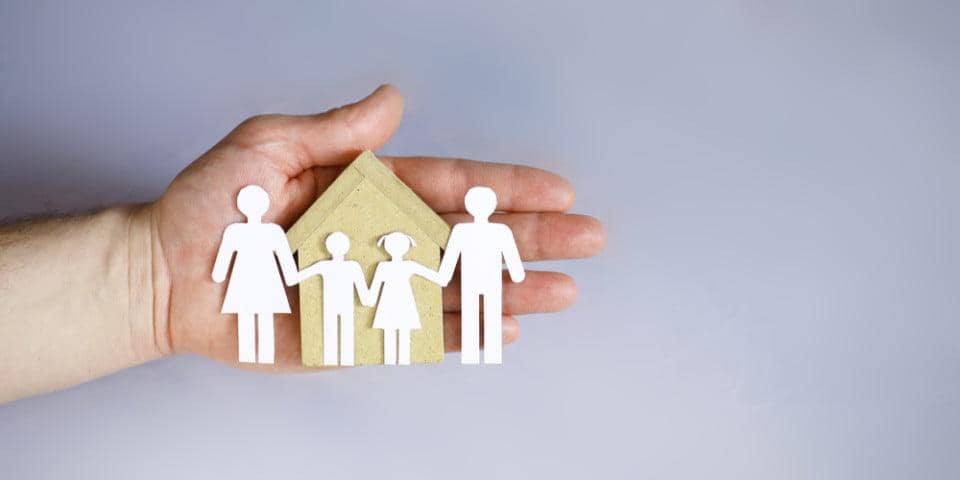 Hand holding paper cutouts of a family and house, representing charitable support for families in need with medical treatment, shopping vouchers, and direct payments, via crypto donations like SOL.