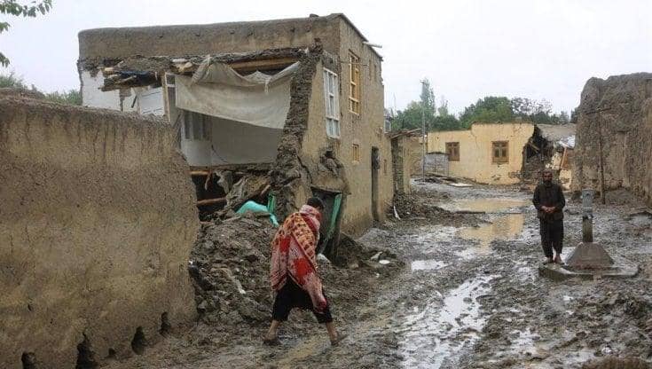 Damaged homes in Afghanistan with people walking through mud, symbol of need for humanitarian aid and crypto donations via USDT.