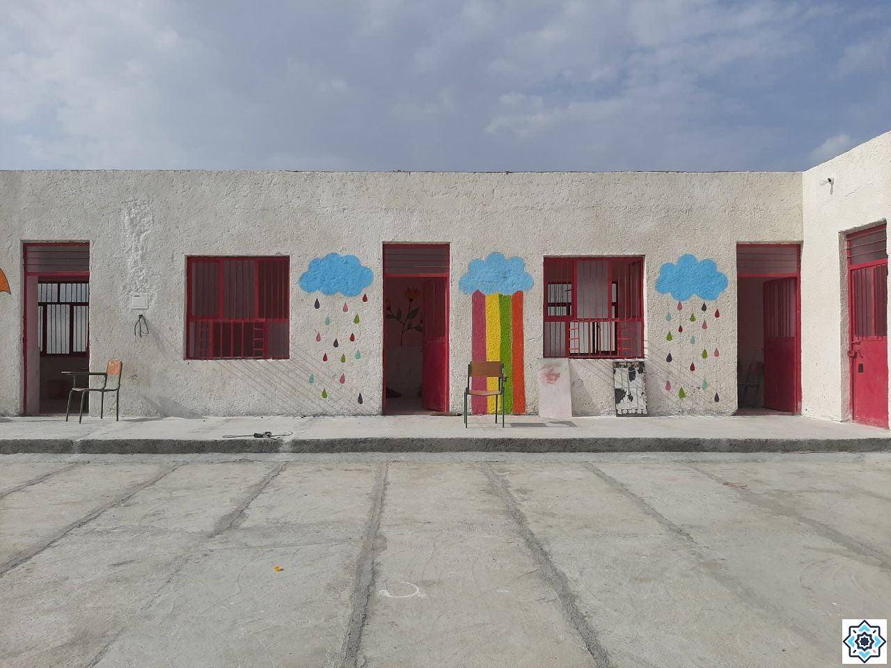 Exterior of a colorful school building with painted clouds and raindrops above windows; cheerful mural signifies hope for children acquiring education through crypto donations, processed via USDT.