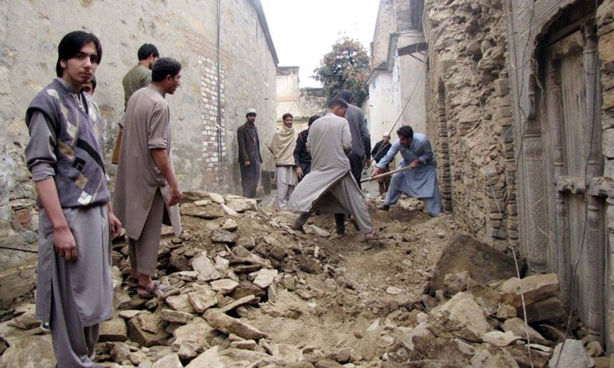 Men clearing rubble after an earthquake in Afghanistan, with a group looking on. Crypto donations like USDT support immediate relief efforts.